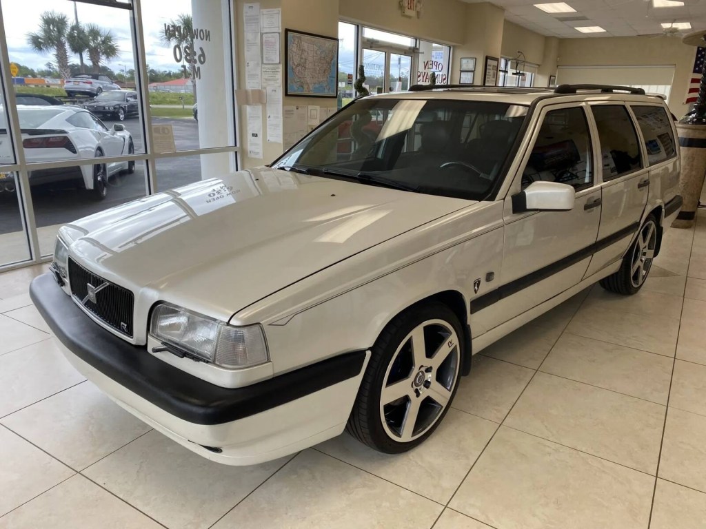 A white metallic 1996 Volvo 850 Turbo Platinum Edition Wagon parked in a dealer showroom in high left front angle view