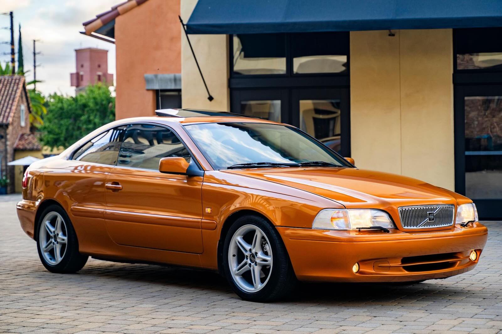 The front of an orange Volvo C70 Grand Touring coupe, parked in front of a house