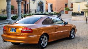 The rear of an orange Volvo C70 coupe parked in front of a house.