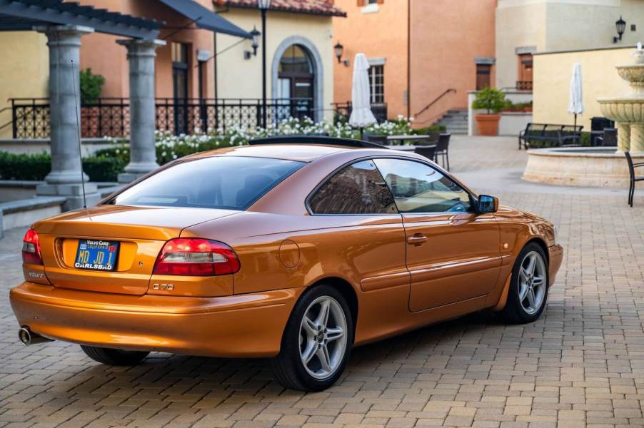 The rear of an orange Volvo C70 coupe parked in front of a house.