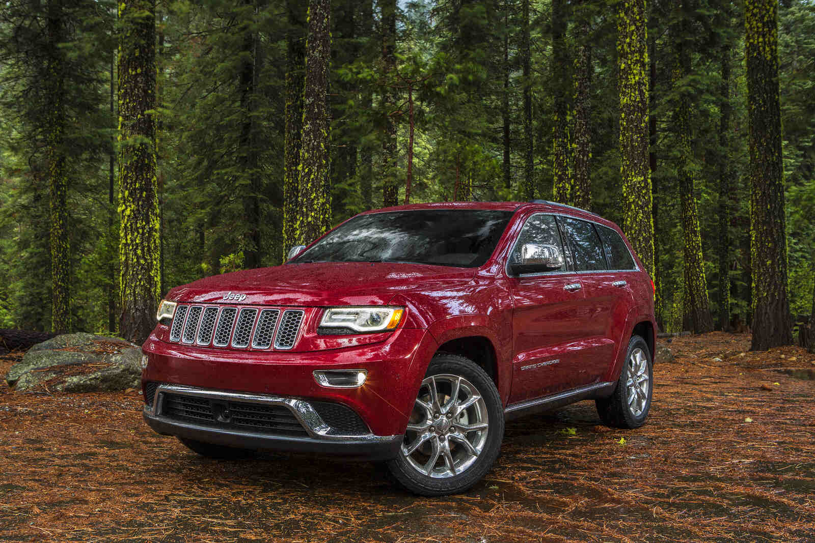A red 2015 Jeep Grand Cherokee parked in the woods in left front angle view