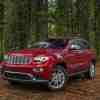 A red 2015 Jeep Grand Cherokee parked in the woods in left front angle view