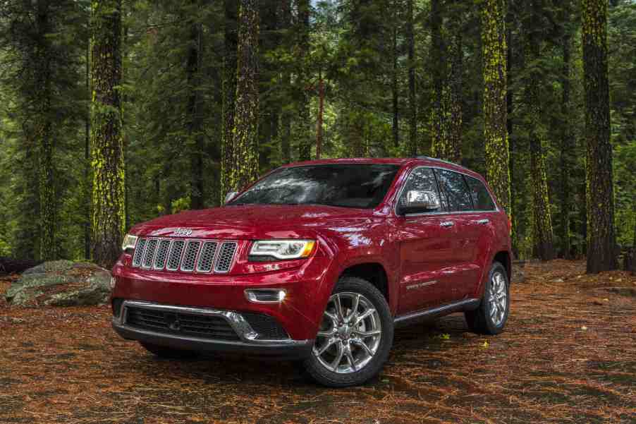 A red 2015 Jeep Grand Cherokee parked in the woods in left front angle view