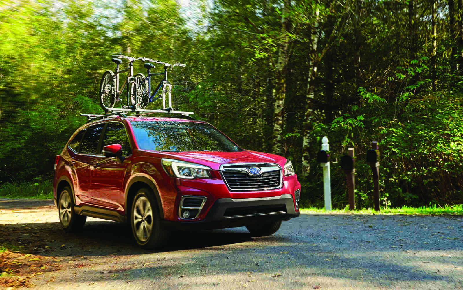 A red 2020 Subaru Forester with a bike roof rack driving uphill in right front angle view