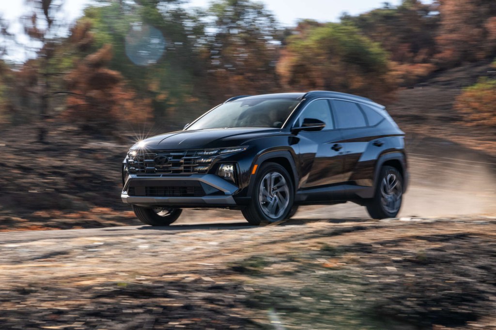 A dark colored 2025 Hyundai Tucson Hybrid driving on an unpaved wooded road in left front angle view