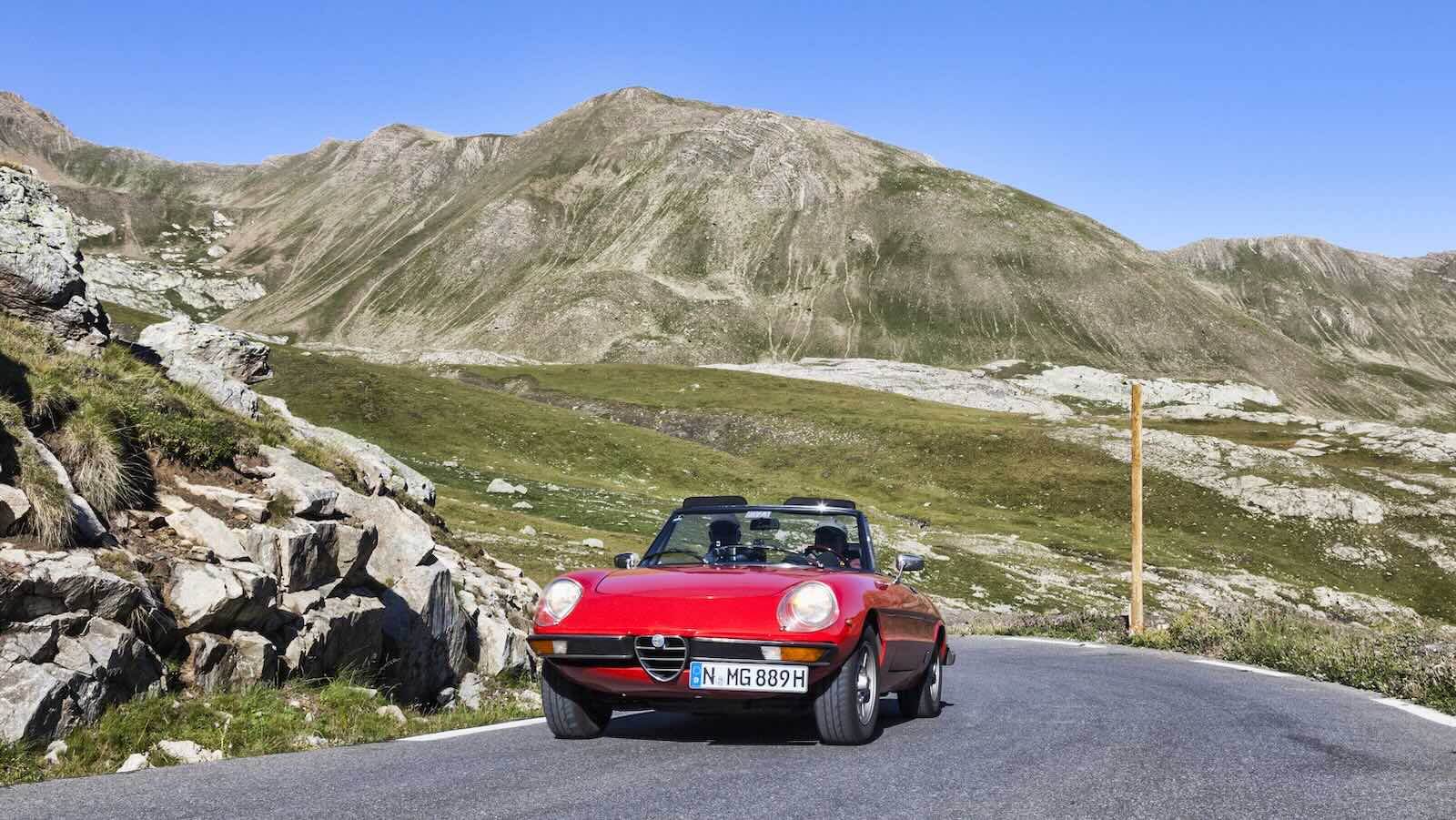 Red Alfa Romeo spider driving on a mountain road.