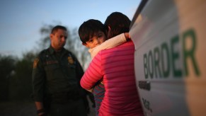 Child holds onto its mother outside a border patrol ICE agent's vehicle during a traffic stop