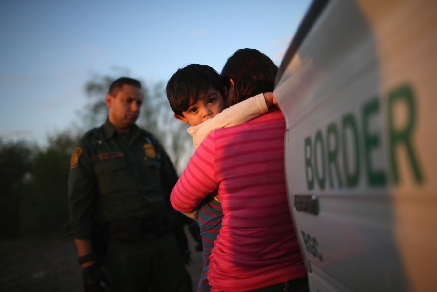 Child holds onto its mother outside a border patrol ICE agent's vehicle during a traffic stop