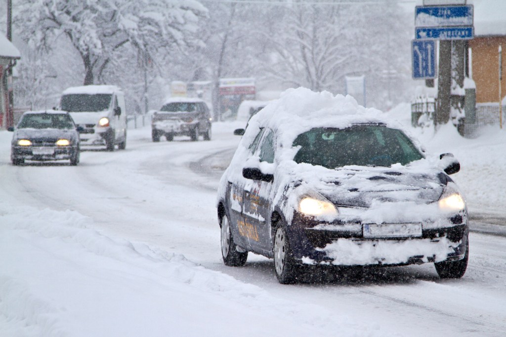 A car in traffic with snow on the roof