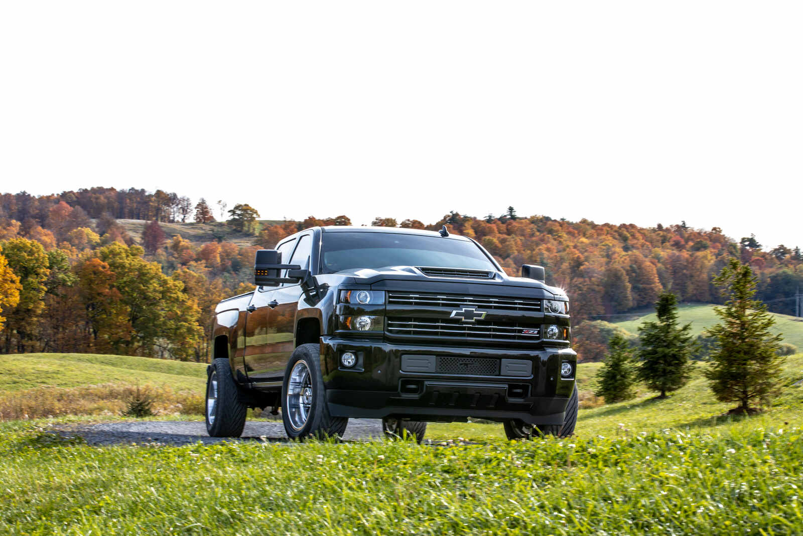 A black Chevrolet Silverado Duramax diesel pickup truck parked on a grassy hill with fall trees in the background