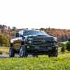 A black Chevrolet Silverado Duramax diesel pickup truck parked on a grassy hill with fall trees in the background