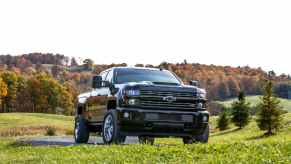 A black Chevrolet Silverado Duramax diesel pickup truck parked on a grassy hill with fall trees in the background