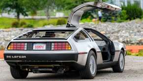 DeLorean sports car parked in a dirt lot with one gullwing door up