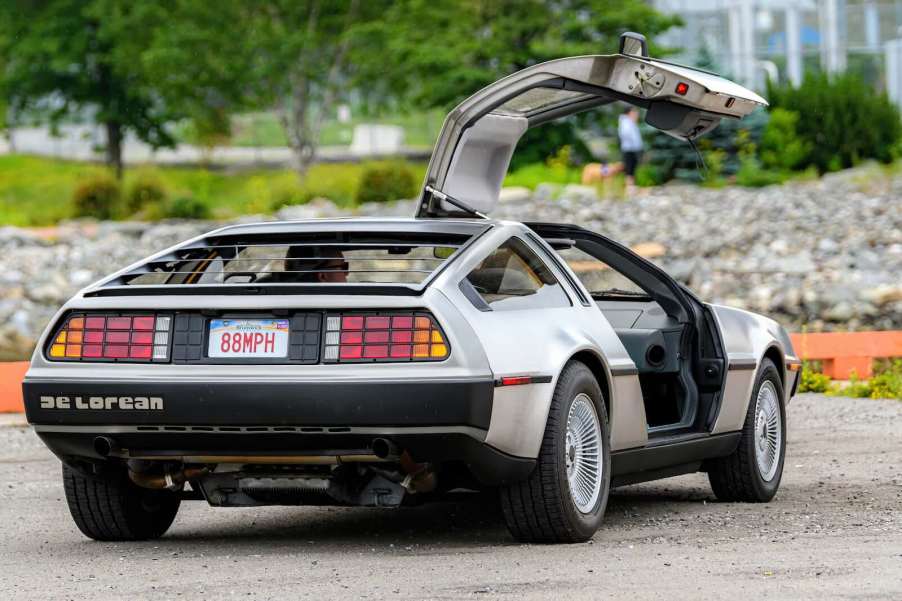 DeLorean sports car parked in a dirt lot with one gullwing door up