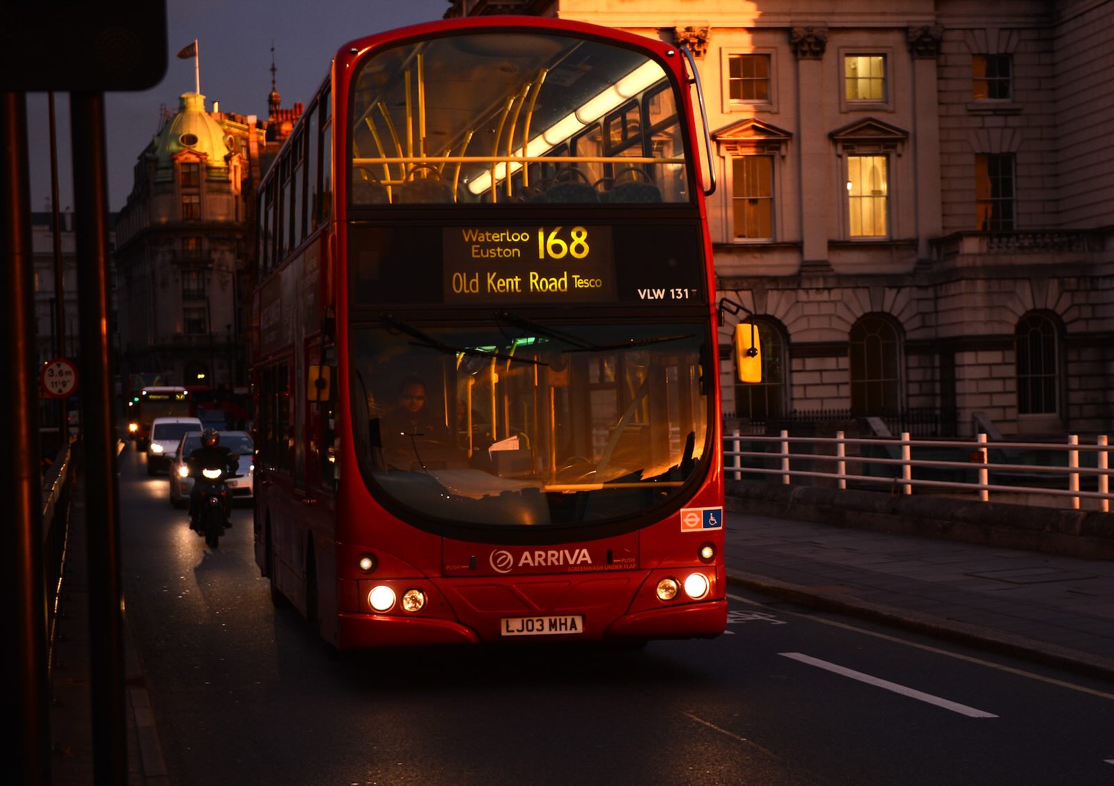 Red double decker UK bus at night.