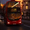 Red double decker UK bus at night.