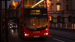 Red double decker UK bus at night.