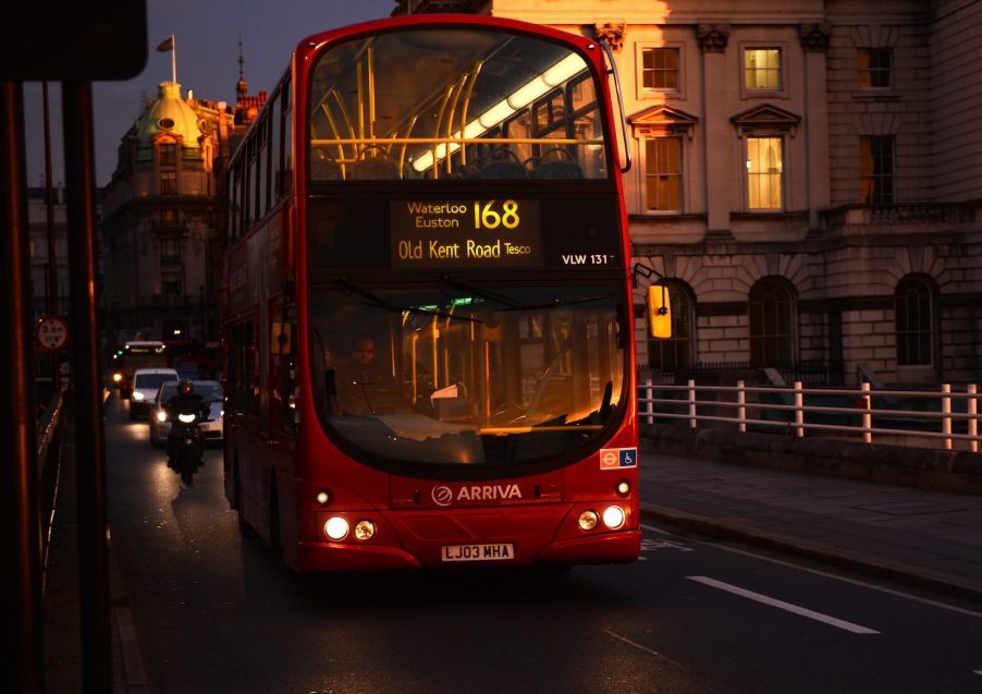 Red double decker UK bus at night.