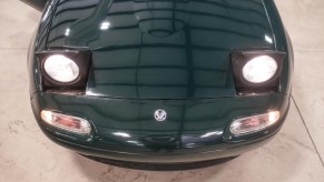 The hood and pop-up headlights of a British Racing Green JDM Eunos Roadster.