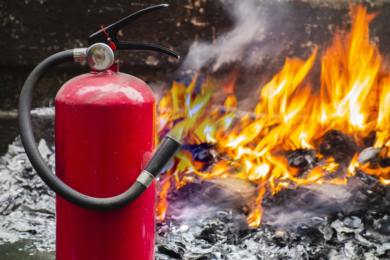 Fire extinguisher in the foreground, flames from a burning Porsche in the background.
