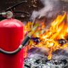 Fire extinguisher in the foreground, flames from a burning Porsche in the background.