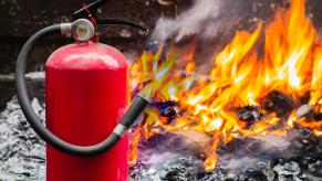 Fire extinguisher in the foreground, flames from a burning Porsche in the background.