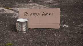 "Please help" cardboard sign and collection cup from a panhandler beggar