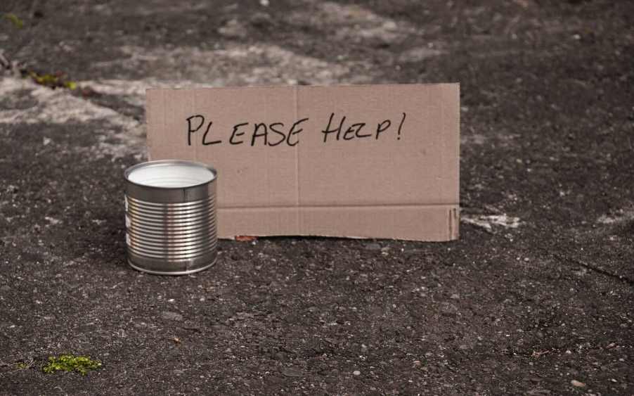 "Please help" cardboard sign and collection cup from a panhandler beggar