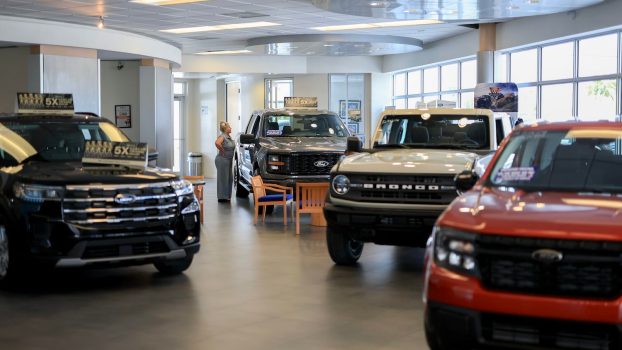 A Ford dealership showroom with a Maverick in the foreground and an F-150 pickup truck in the background.