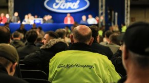 Factory workers look at a Ford sign on a stage during a meeting.