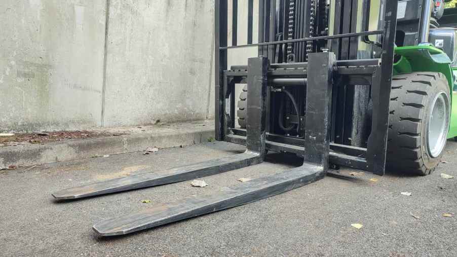 The forks of a green forklift sitting on the pavement.