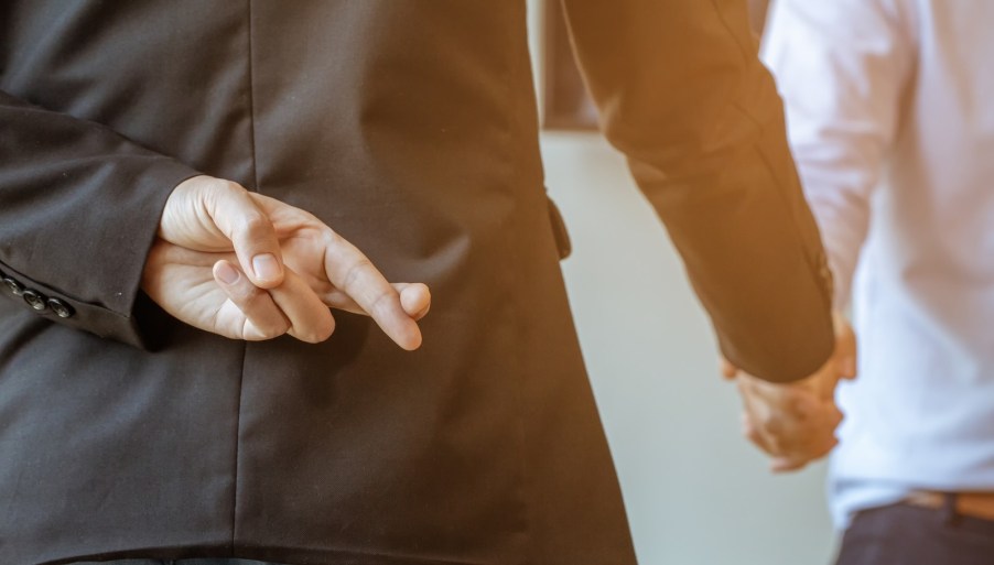 Man in suit with his fingers crossed shakes hands