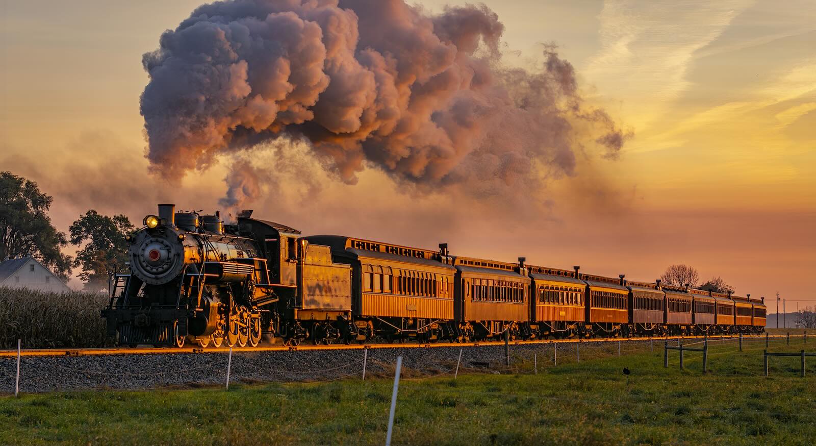 Steam locomotive on train tracks, fields in the foreground.