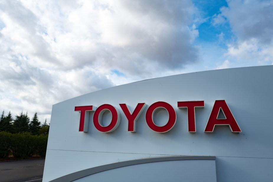 The Toyota logo on a dealership sign, trees and blue sky in the background.