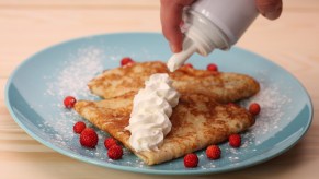 Someone sprays whipped cream from a can onto pancakes.