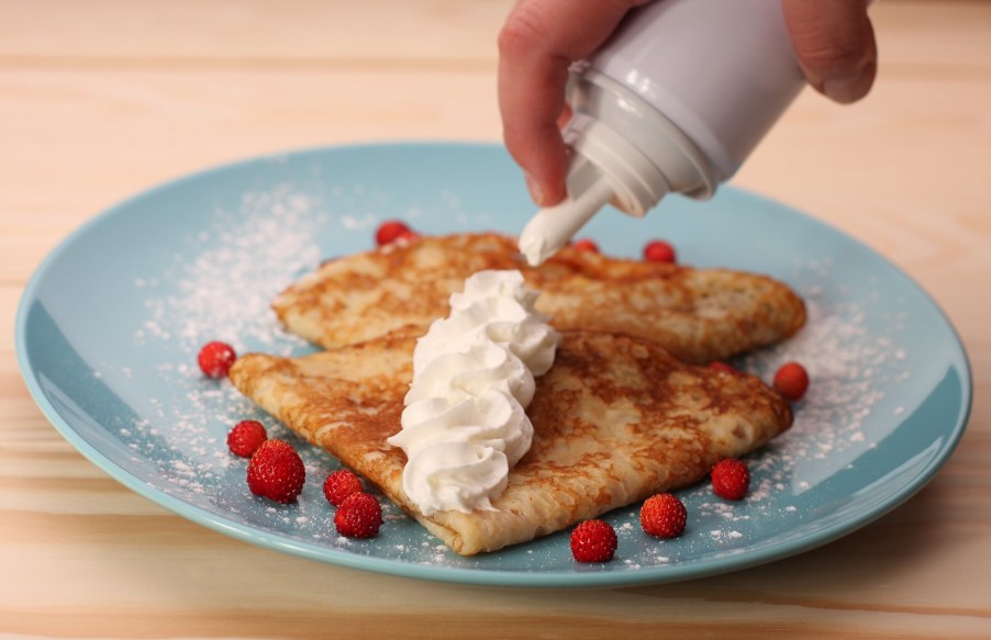 Someone sprays whipped cream from a can onto pancakes.