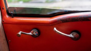 The chrome window crank and door latch on a metal red car door.