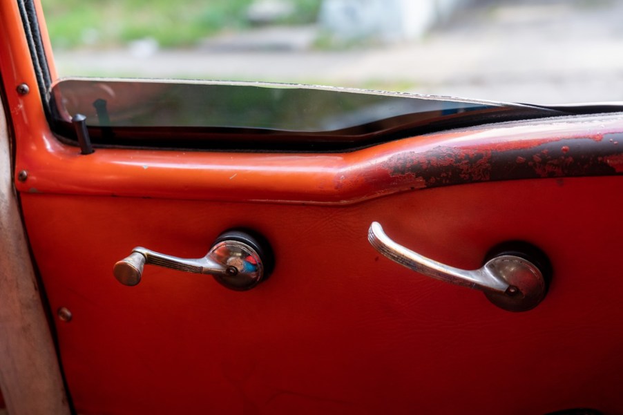 The chrome window crank and door latch on a metal red car door.