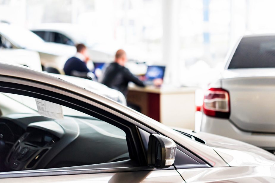 A blurred car dealership showroom with two salespeople sitting in the midground facing away