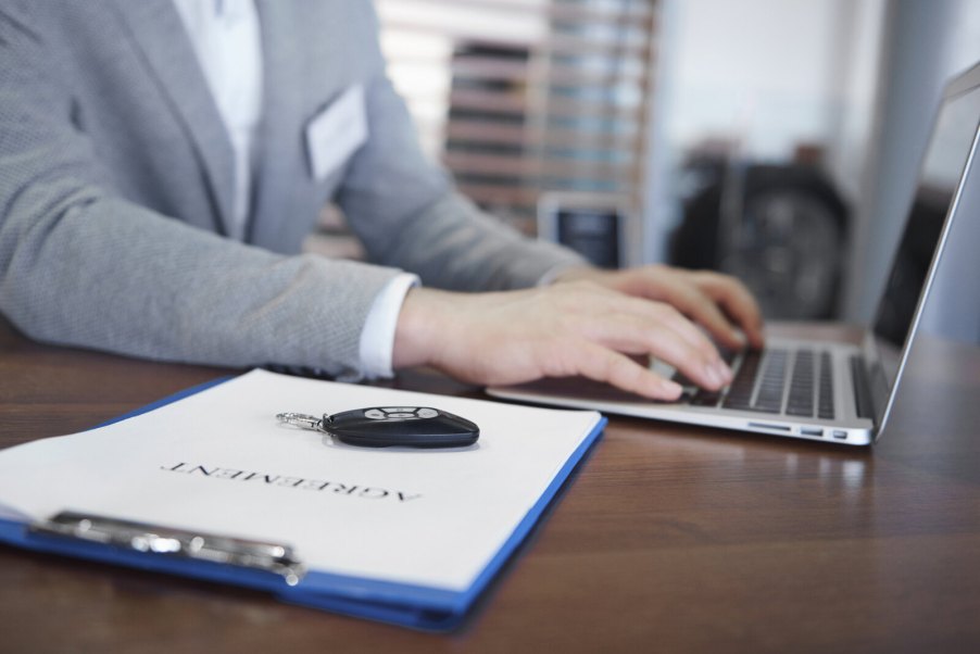 A car dealer salesperson works on laptop in close view