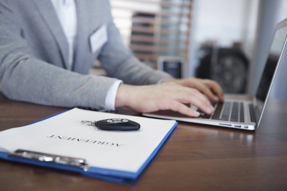 A car dealer salesperson works on laptop in close view