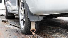 A silver car strapped to tow flatbed truck in close low left rear view