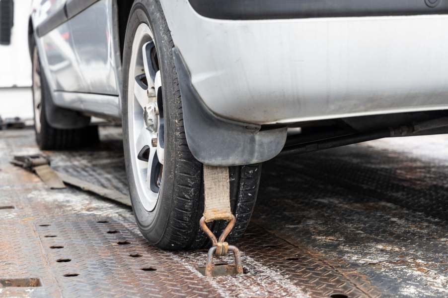 A silver car strapped to tow flatbed truck in close low left rear view