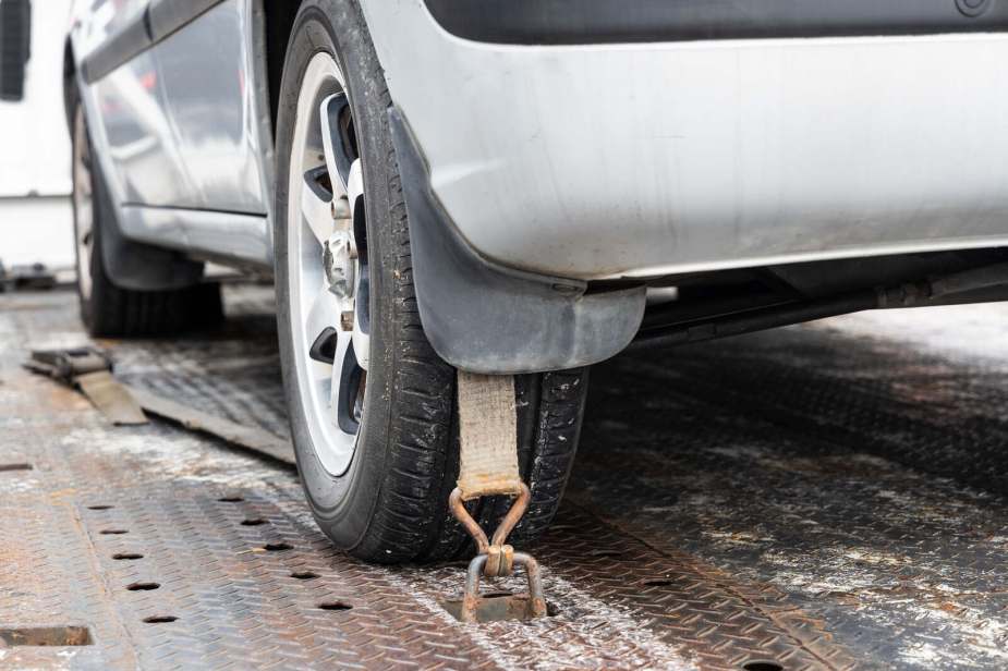 A silver car strapped to tow flatbed truck in close low left rear view