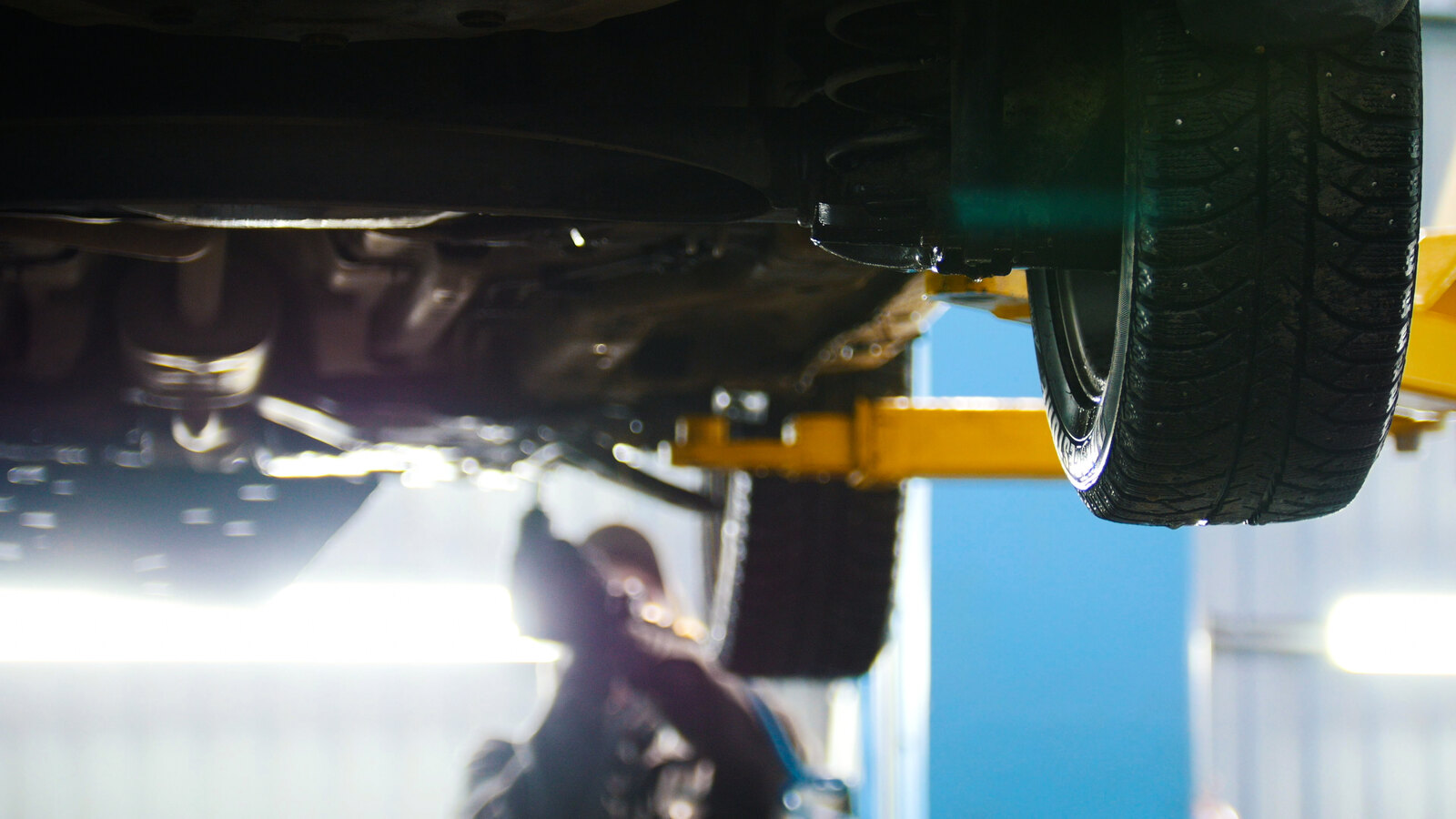 A car on a two-post lift with a mechanic under it