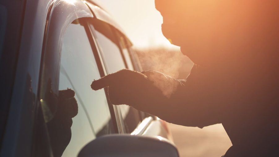 A masked and gloved carjacker points at a driver in close view