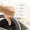 A driver gives the "thumbs-down" signal in close view of his hand and steering wheel
