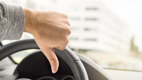 A driver gives the "thumbs-down" signal in close view of his hand and steering wheel