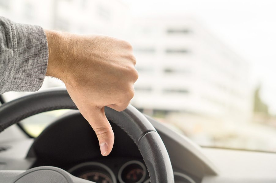 A driver gives the "thumbs-down" signal in close view of his hand and steering wheel