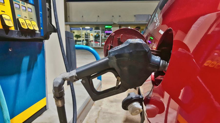 A red car gets filled up at a gas station in close view of the nozzle
